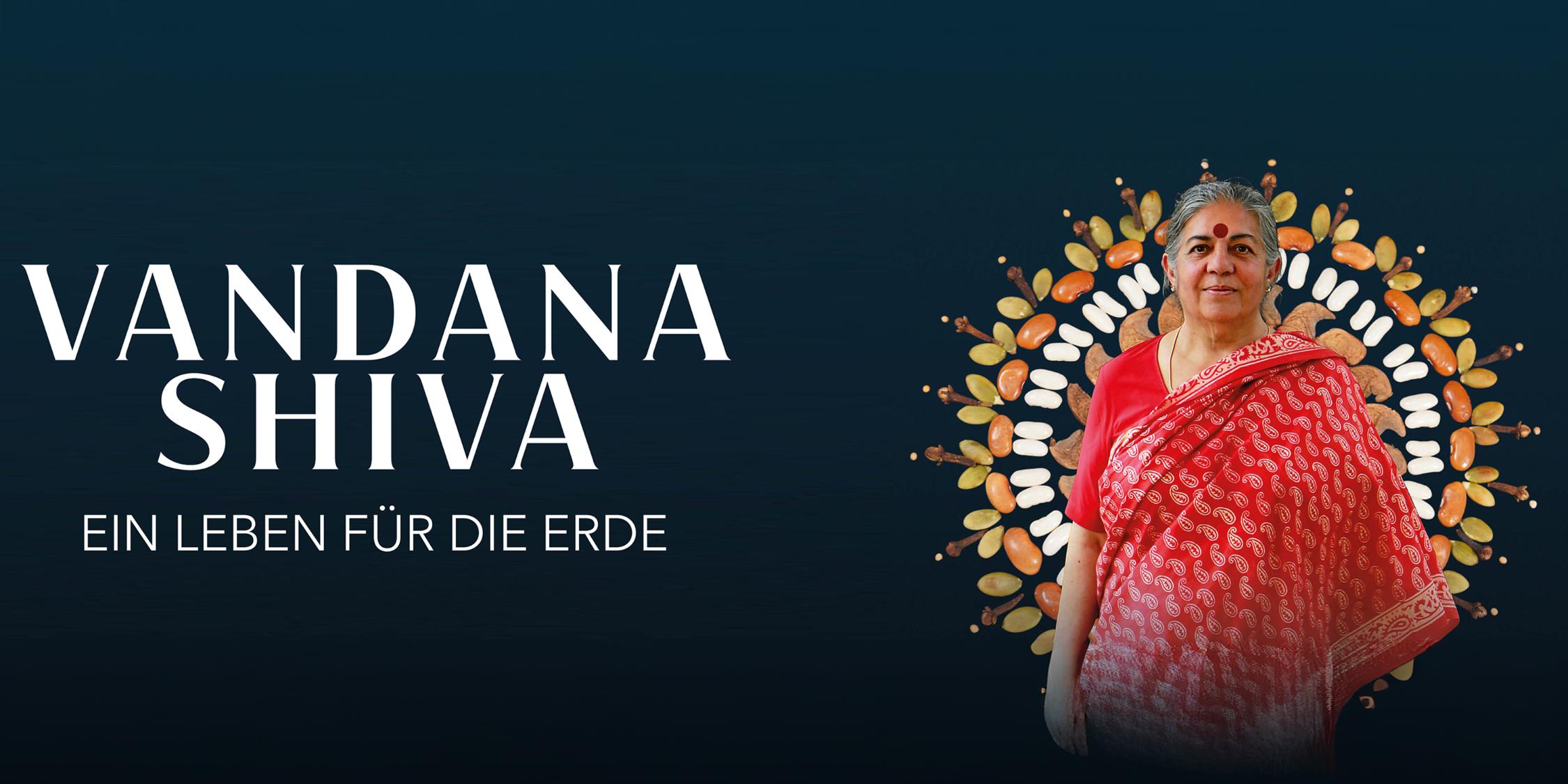 Eine Frau in einem roten Sari und mit rotem Punkt auf der Stirn lächelt in die Kamera.