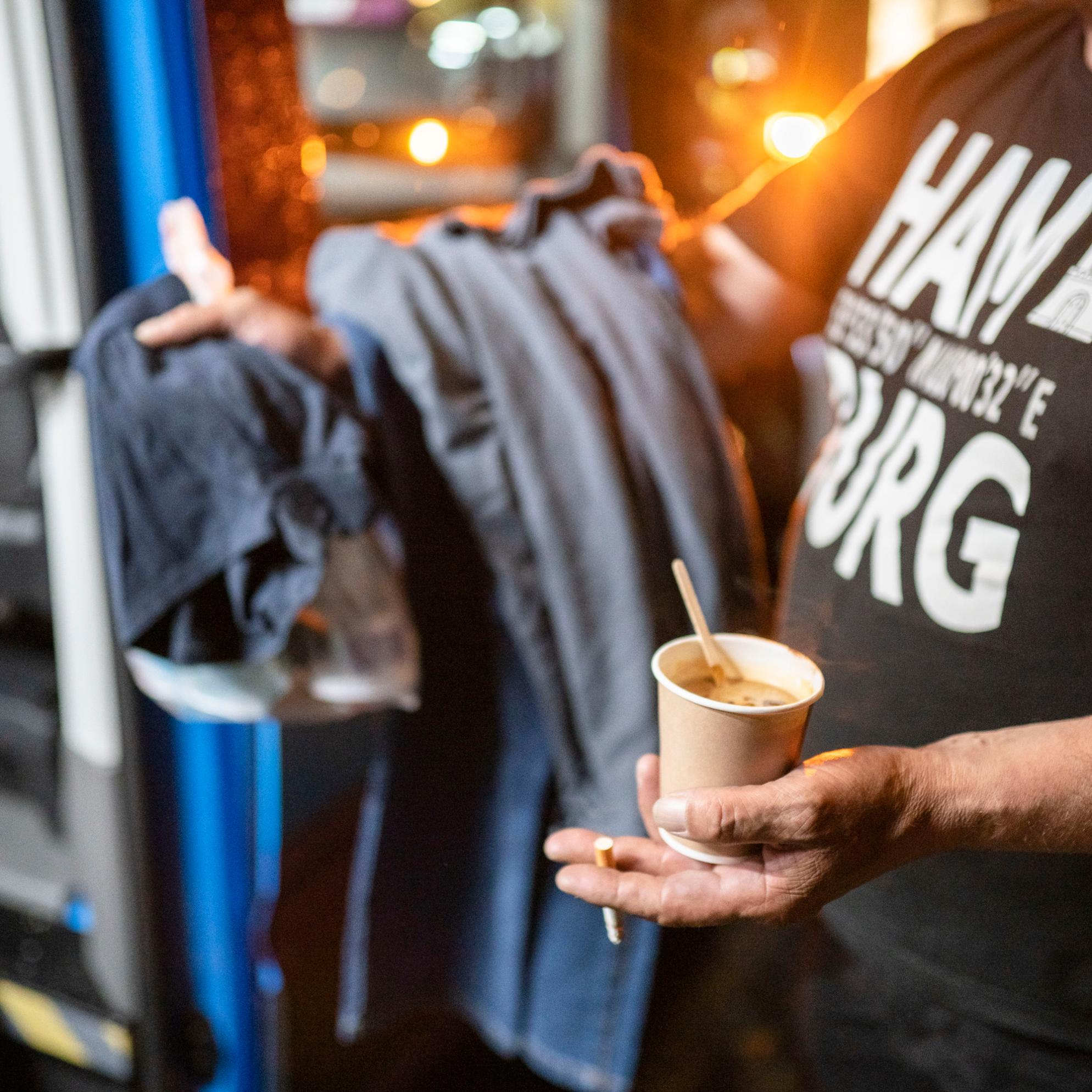 Ein Mann hält einen Kaffeebecher und eine Zigarette in der Hand.