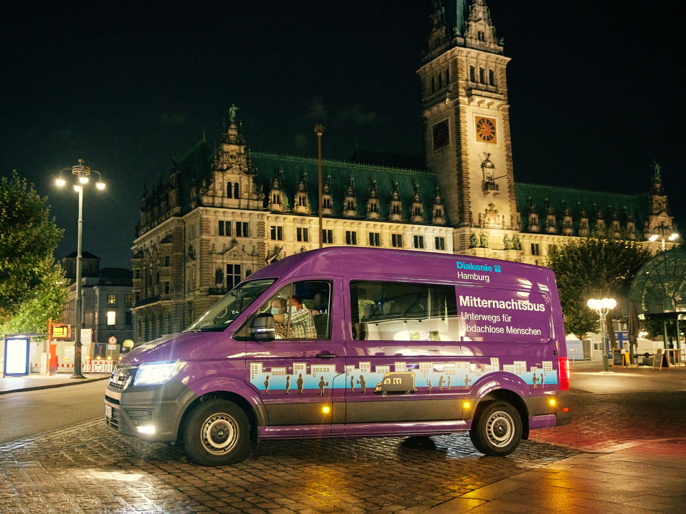 Der lilafarbene Mitternachtsbus steht vor dem Hamburger Rathaus bei Nacht.