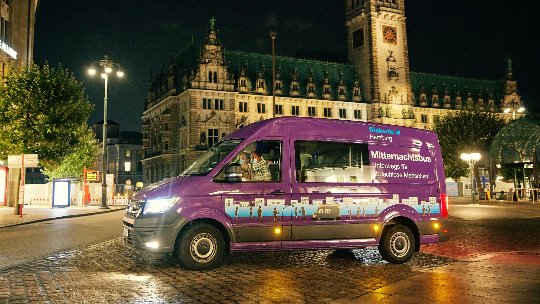 Der lilafarbene Mitternachtsbus steht vor dem Hamburger Rathaus bei Nacht.