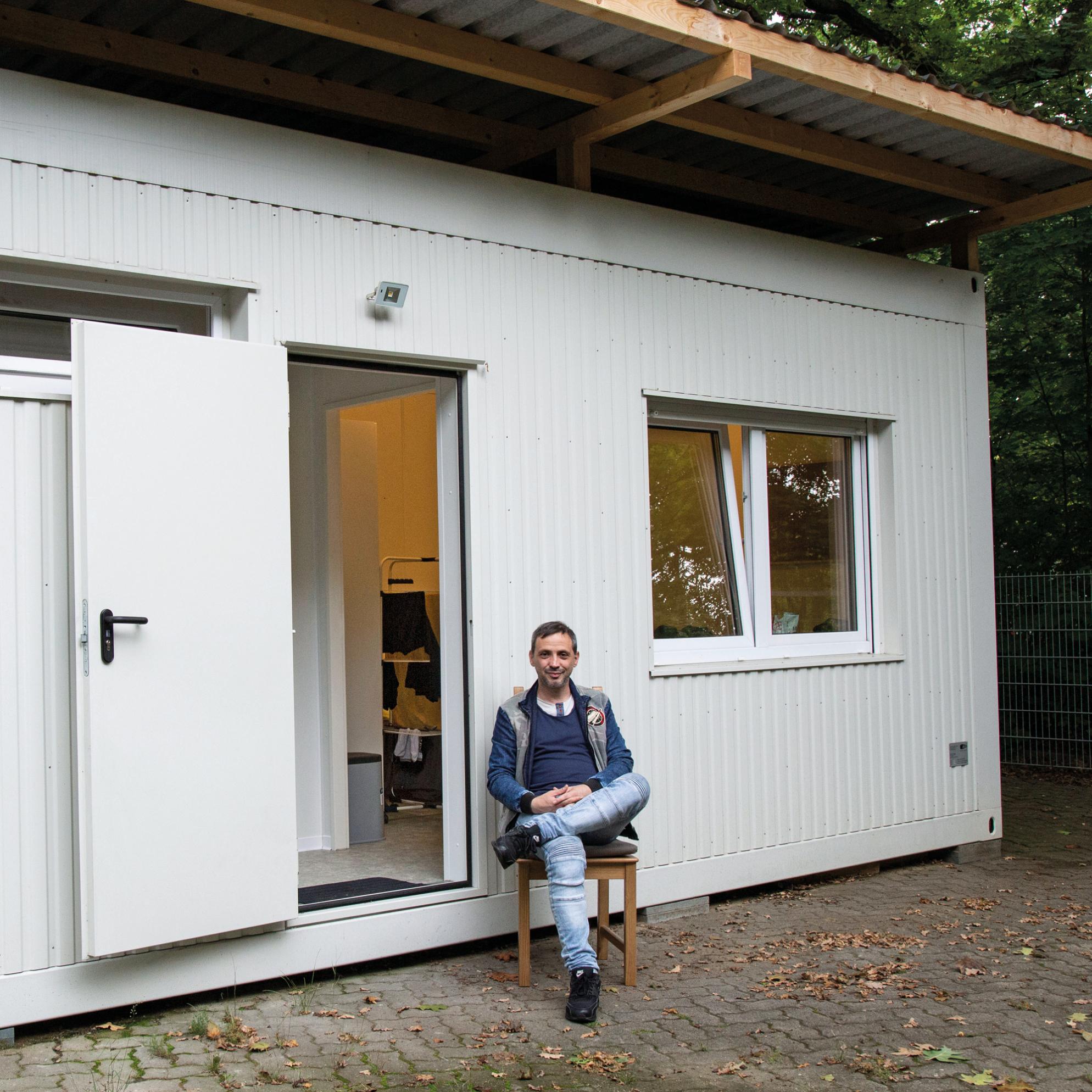Ein Mann sitzt auf einem Stuhl vor einem weißen Containerhaus.