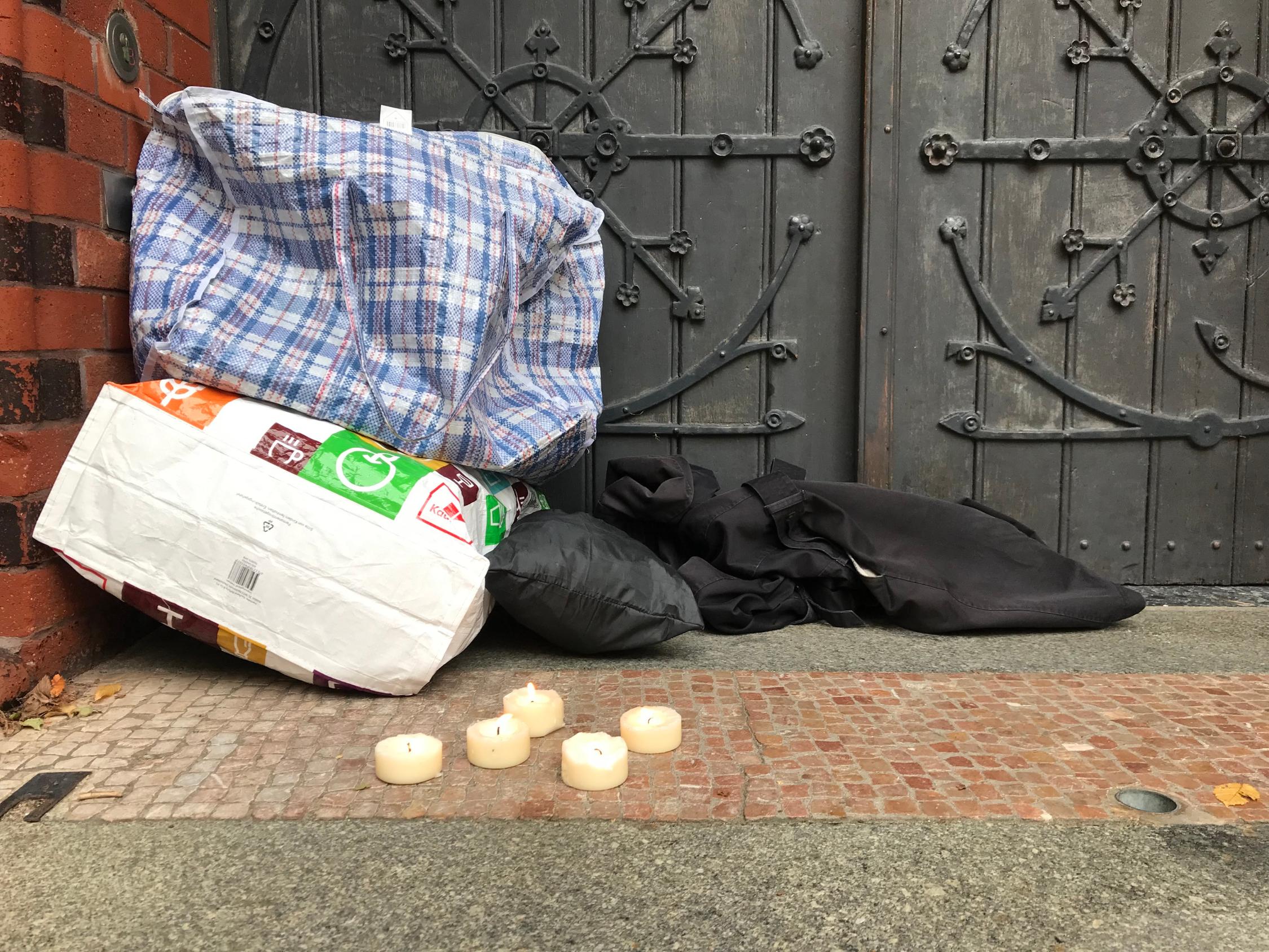 Große Einkaufstaschen liegen vor einem Tor und davor stehen brennende Teelichter.